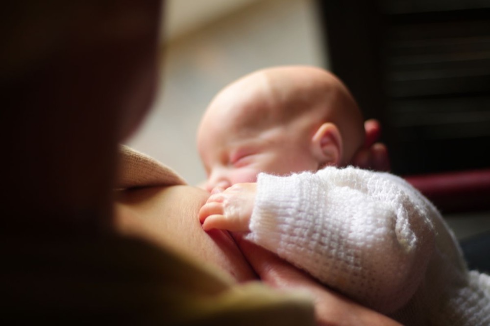 Mẹ cho con bú, bàn tay bé nắm lấy ngực mẹ